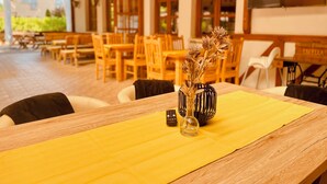 A wooden table with a yellow placemat, a vase with dried flowers, and a remote control. - Sommer Pension (Balatonfoldvar)