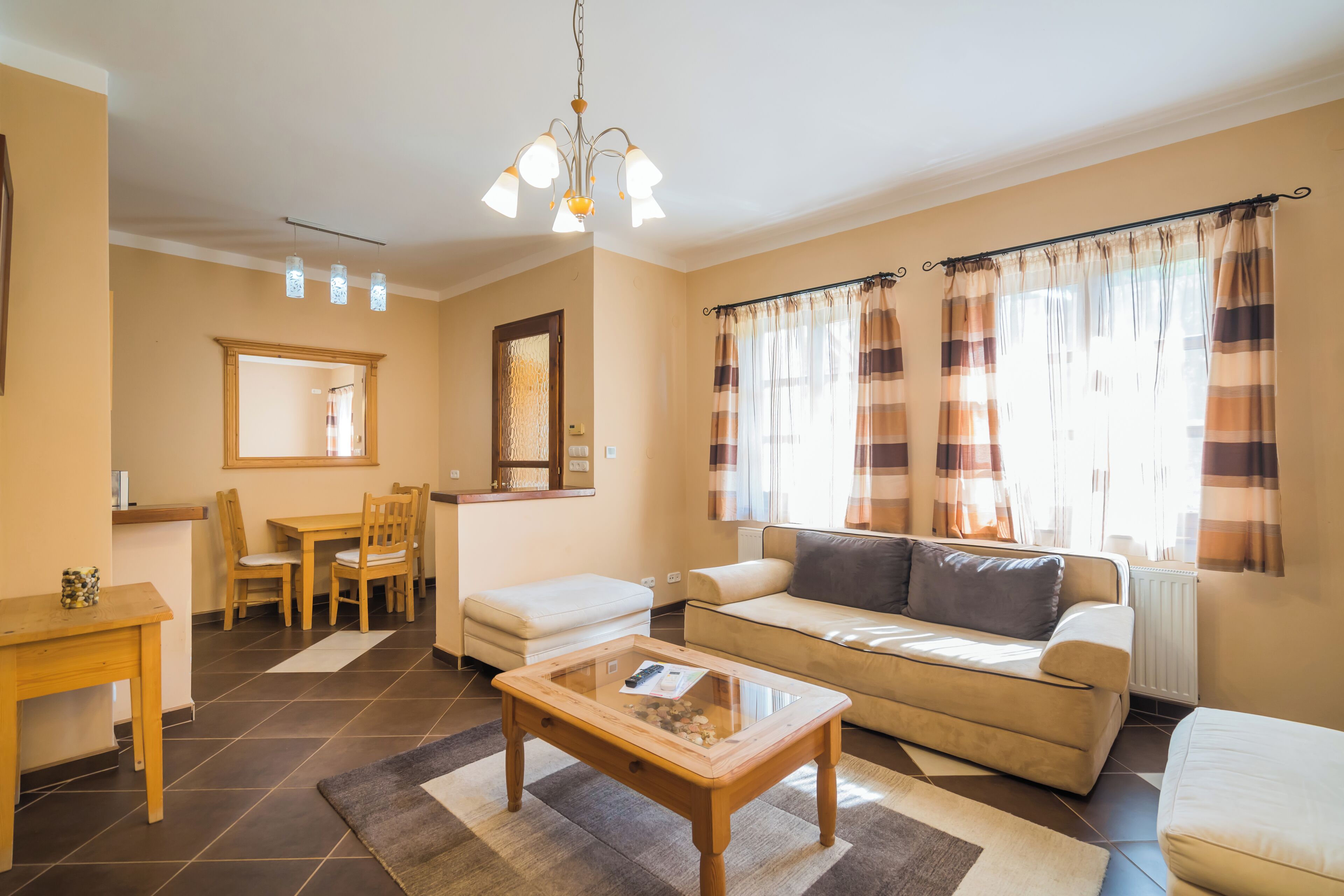 Een woonkamer met een bank, een salontafel, een eettafel met stoelen en een kroonluchter.