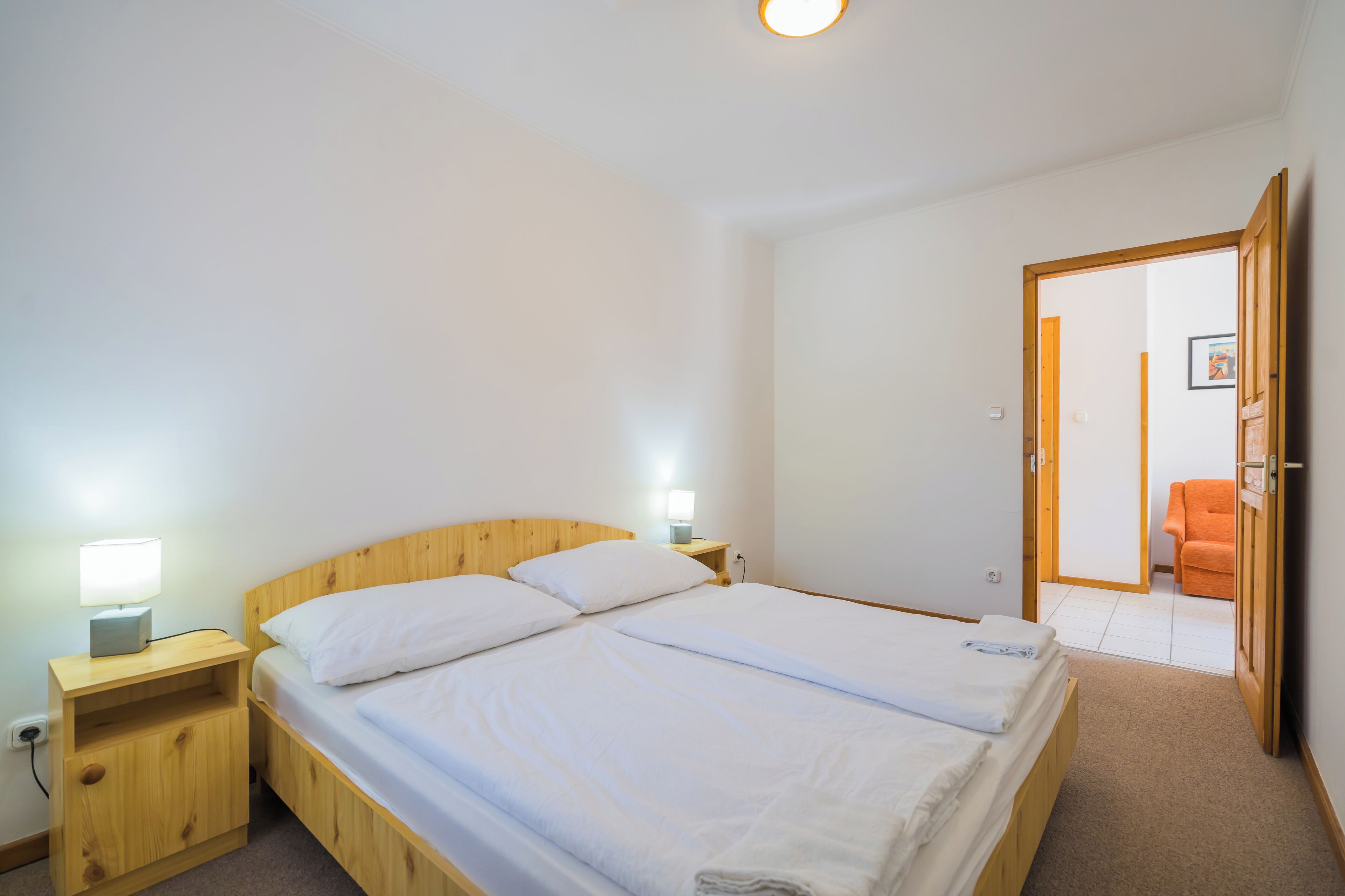 Ein Doppelbett mit weißen Bettwäsche, ein Holzkopfende und Nachttische mit Lampen.