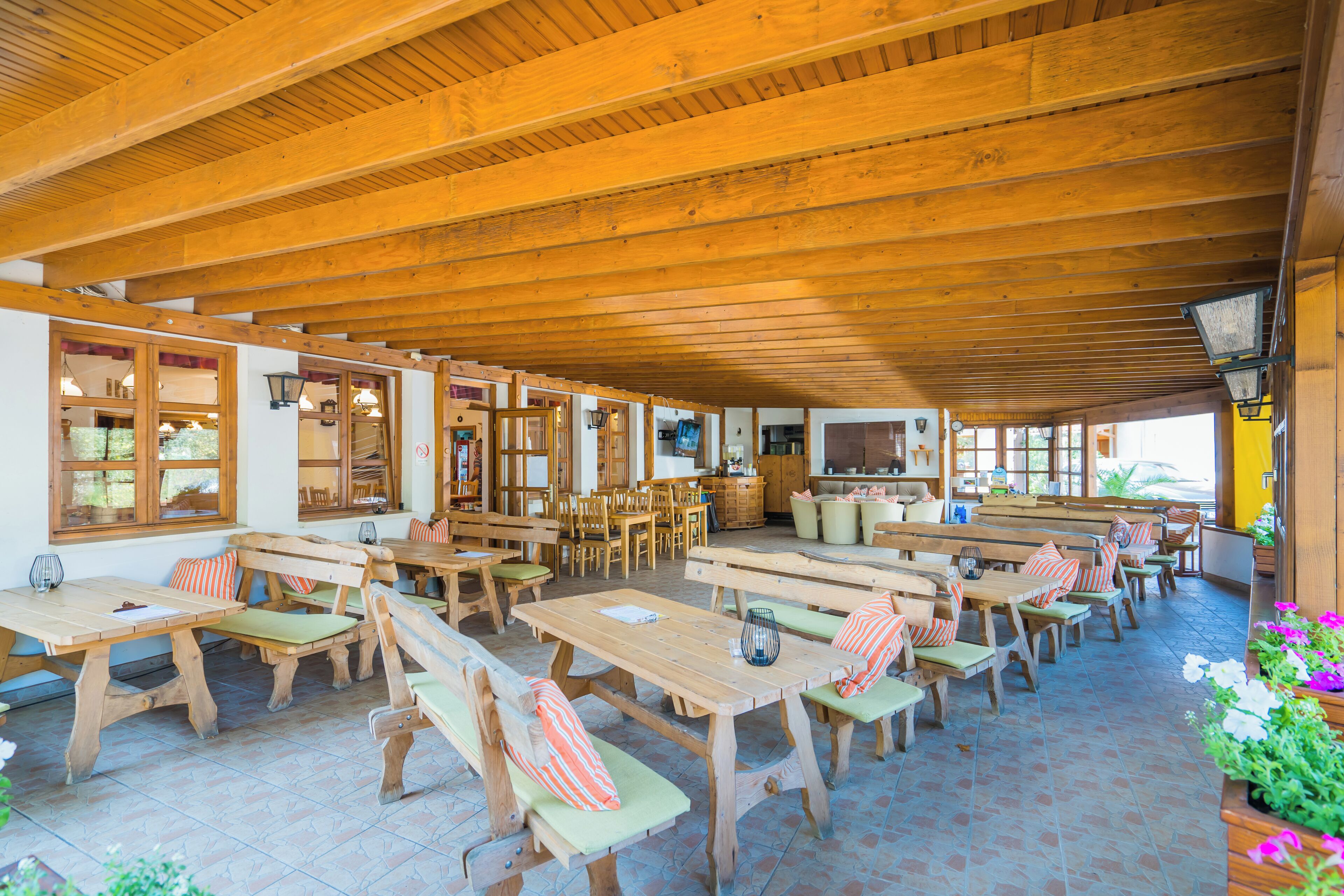 Un café al aire libre con mesas y bancos de madera, piso de baldosas y techo de madera.