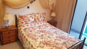 Un dormitori amb estovall de flors, dues taules de nit amb làmpades, un taulell de nit de fusta i una finestra amb cortines.
