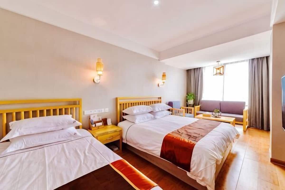 Ein Hotelzimmer mit zwei Betten, einem Sofa, einem Fernseher und einem Fenster mit Vorhängen.