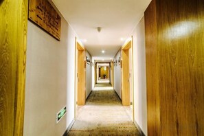 A hotel corridor with wooden doors, a carpeted floor, and a sign on the wall. - Xiao Jing Hotel (Anji)