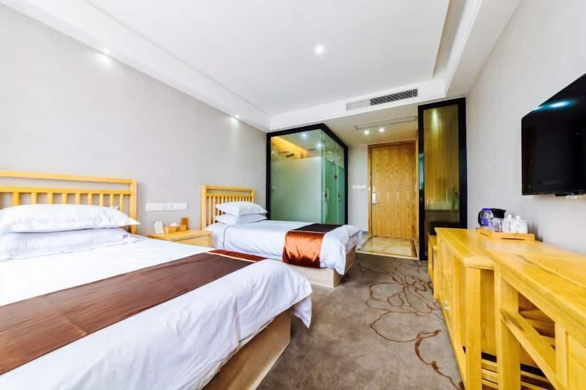Ein Hotelzimmer mit zwei Betten, einem Holztisch, einem Fernseher und einer Glastür zum Badezimmer.