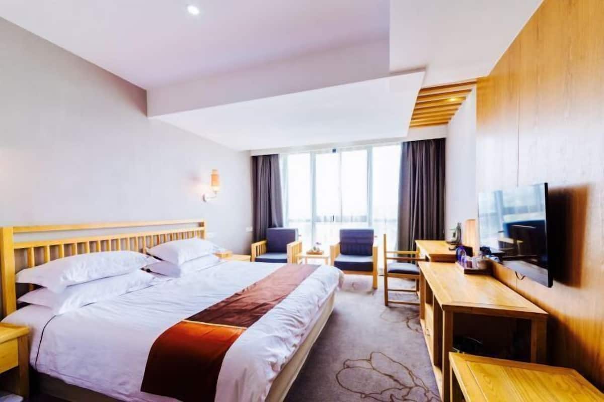 Ein Hotelzimmer mit einem großen Bett, einem Schreibtisch, einem Sessel, einem Fernseher und einem Fenster mit Vorhängen.