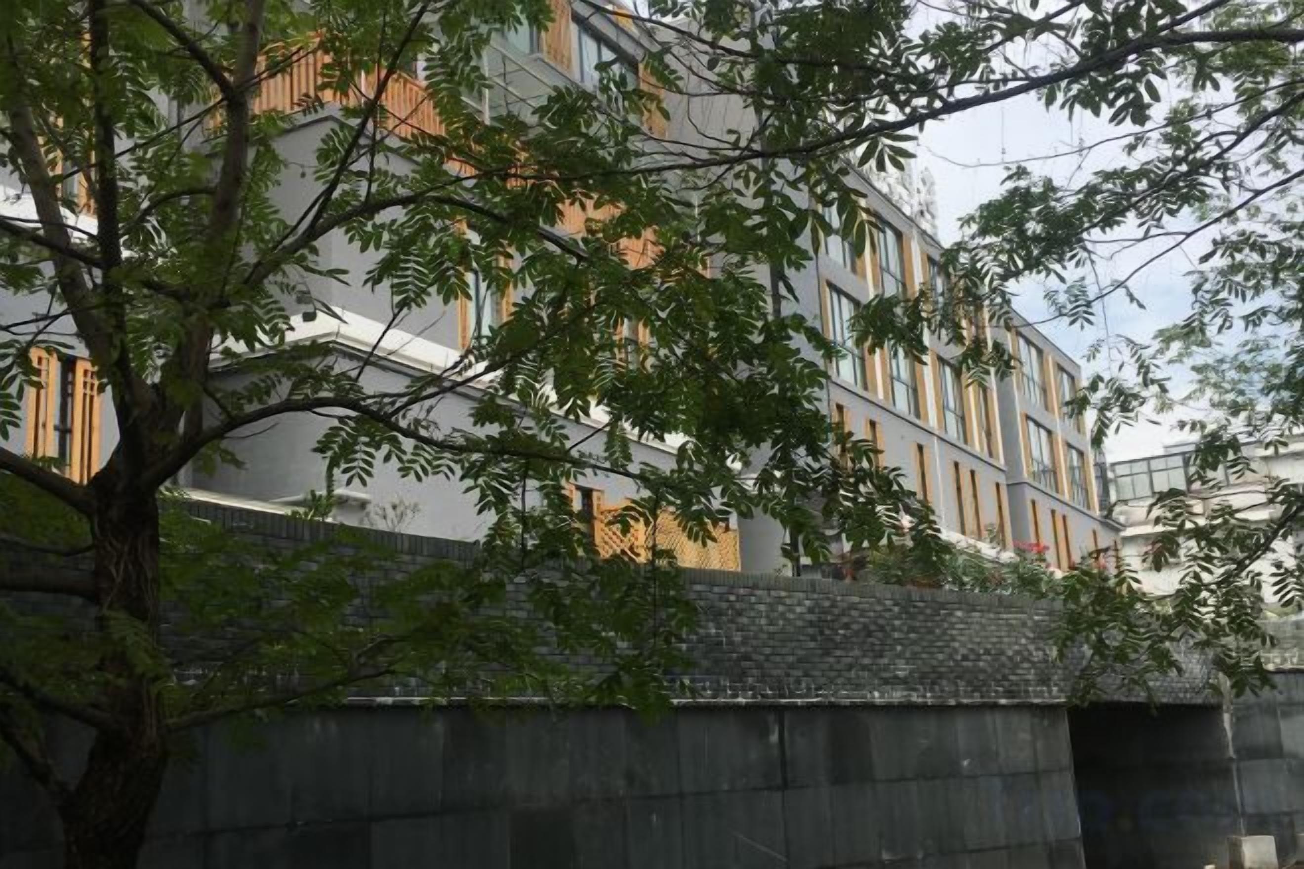A multi-story building with a modern architectural design, featuring a balcony and a tree in the foreground.
