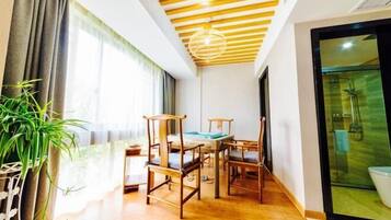A room with a wooden dining table, chairs, a hanging light fixture, and a large window with curtains.