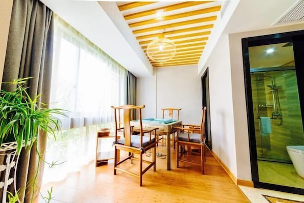 A room with a wooden dining table, chairs, a hanging light fixture, and a large window with curtains. - Xiao Jing Hotel (Anji)