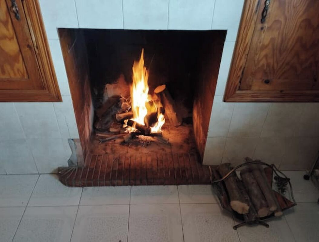 Een haard met brandhout, een betegelde vloer en houten kastjes.