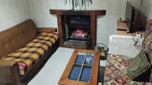 A living room with a brown sofa, a patterned rug, a fireplace, and a television. - La Casa del Río, natural pool 5 min by car (Villacarrillo)