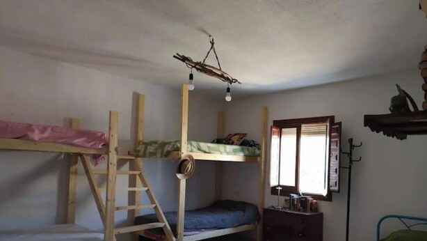 A room with two bunk beds, a ladder, a small desk, a window with blinds, and a hanging light fixture. - La Casa del Río, natural pool 5 min by car (Villacarrillo)