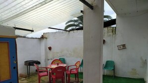 A covered outdoor area with a table and chairs, a blue door, and a white wall with a small picture. - La Casa del Río, natural pool 5 min by car (Villacarrillo)