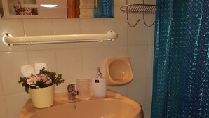 Et badeværelse med et væghængt håndvask, en lille trinbænk, en håndklædeholder og en dekorativ plante.
