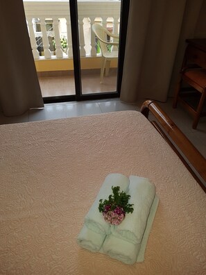 A hotel room with a bed, a wooden headboard, a balcony with a white chair, and a wooden table.