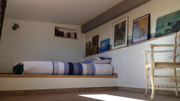 A bedroom with a bed, a wooden chair, and artwork on the walls. - Apartment @typique (Vieux Port) (La Ciotat)