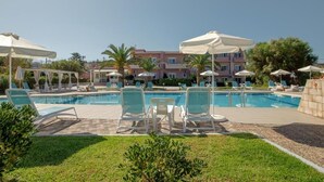 A pool area with lounge chairs and umbrellas, surrounded by a well-maintained lawn and buildings in the background. - SEA SIDE (Chania)