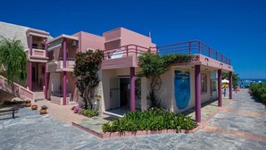 A pink building with a pool area, a staircase, and a view of the sea. - SEA SIDE (Chania)