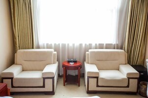 Una habitación con dos sillones color beige, una pequeña mesita de madera y un ventanal con cortinas.