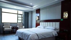 Ein Hotelzimmer mit einem großen Bett, zwei Sesseln, einem kleinen Tisch und einem Fenster mit Vorhängen.