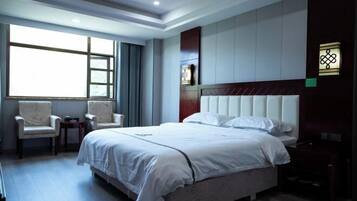 A hotel room with a large bed, two armchairs, a small table, and a window providing natural light.