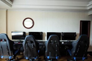 Una sala de juegos con cuatro sillas ergonómicas negras, dos monitores grandes y un espejo con marco de madera en la pared.