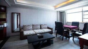 Ein modernes Hotelzimmer mit einer Couch, einem Couchtisch, einem Esstisch mit Stühlen, einem großen Spiegel und einem Fenster mit Vorhängen.