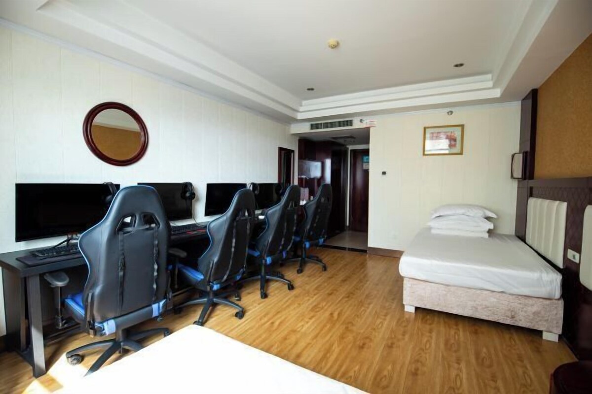 A hotel room with a desk, multiple gaming chairs, a bed, a TV, and a mirror.