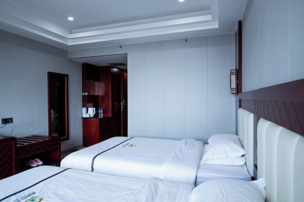 A hotel room with two beds, a wooden headboard, a small desk, and a wardrobe.