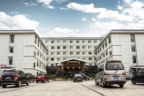 A large building with a central entrance, multiple cars parked in front, and a clear sky. - Yarui Holiday Garden Hotel (Guangshui)