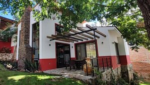 Una casa a due piani con facciata rosso e bianco, una scala in pietra e un pergolato sopra l'ingresso.