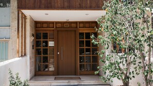 A wooden front door with a glass panel, a potted tree, and a stone pathway leading to the entrance. - Stellar 3BR Apartment with Balcony (Palaio Faliro)
