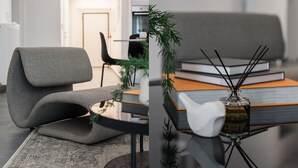 A modern living room with a grey sofa, a small table with books and a decorative bottle, and a door in the background. - Stellar 3BR Apartment with Balcony (Palaio Faliro)