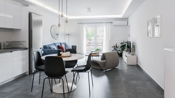 A modern kitchen with a dining area, featuring a large refrigerator, a round dining table with chairs, and a sofa. - Stellar 3BR Apartment with Balcony (Palaio Faliro)