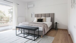 A modern bedroom with a bed, bench, and a view of the outdoors. - Stellar 3BR Apartment with Balcony (Palaio Faliro)