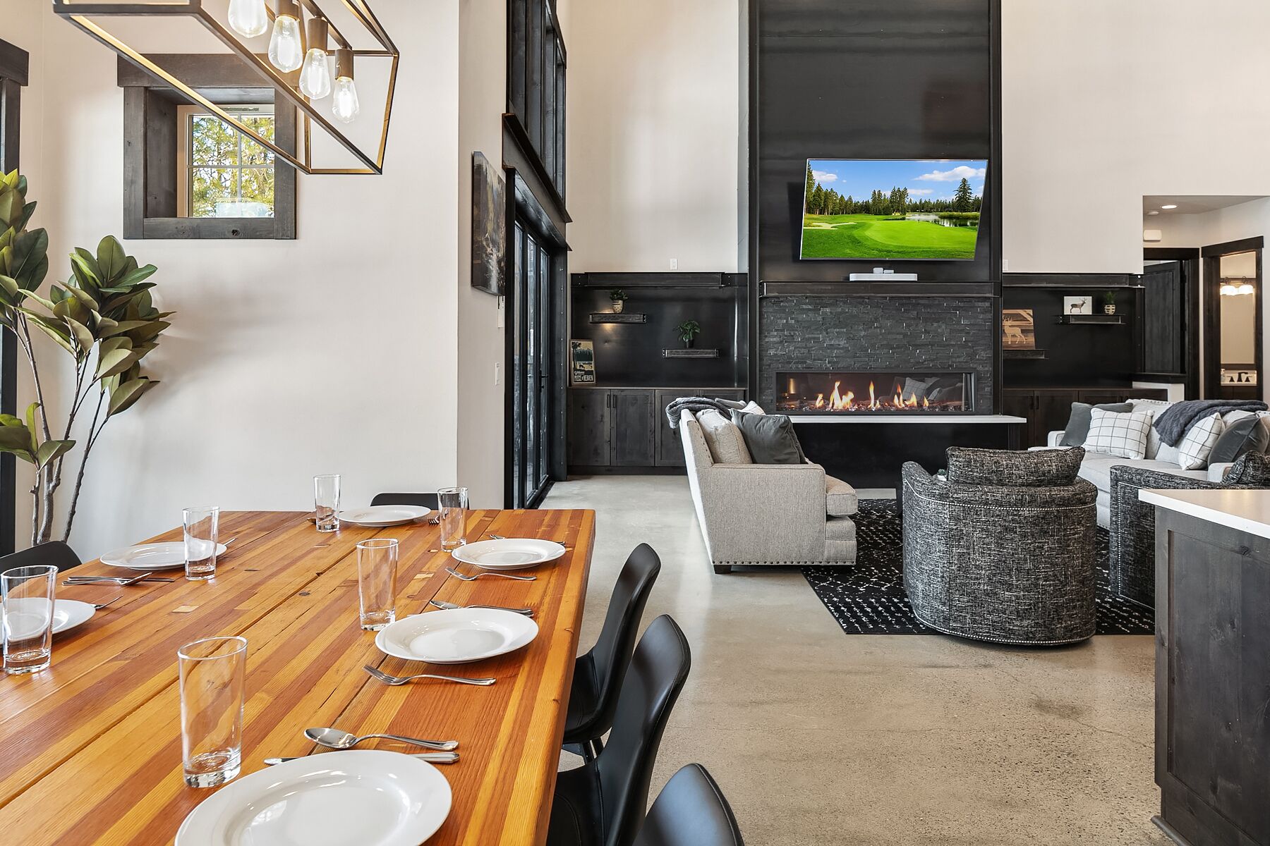 A modern living room with a fireplace, a dining area with a wooden table, and a television displaying a golf course.