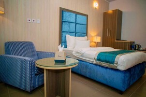 Habitación de hotel con cama, un sillón tapizado en azul, una mesita redonda con una caja de pañuelos y un armario.
