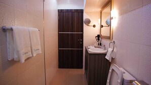 A narrow bathroom with a toilet, sink, and mirror. There are towels hanging on the wall. - Riviera Suites (Lagos)