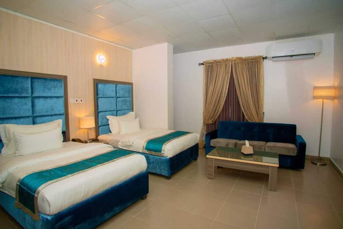 A hotel room with two beds, a sofa, a coffee table, and an air conditioning unit.