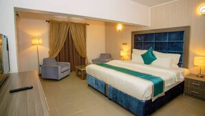 A hotel room with a large bed, a desk, a chair, a TV, and a lamp. - Riviera Suites (Lagos)