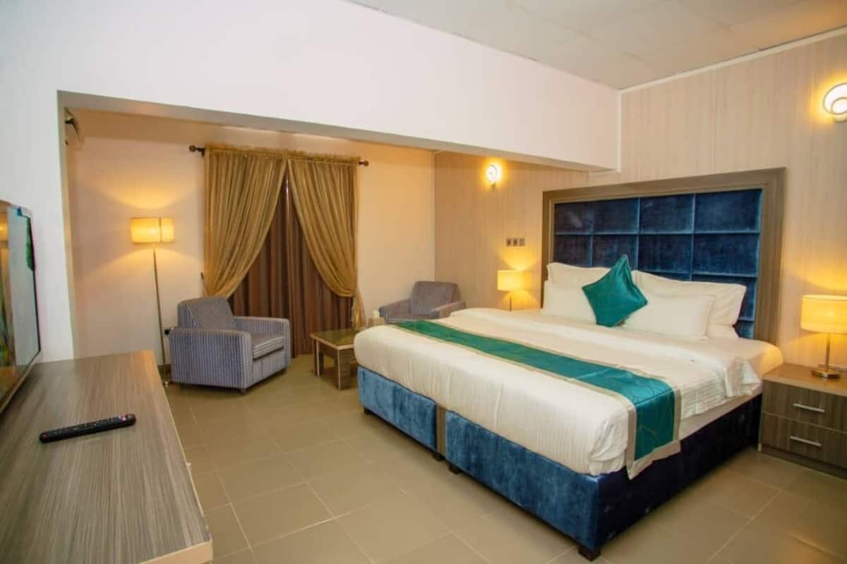 A hotel room with a large bed, a desk, a chair, a TV, and a lamp.