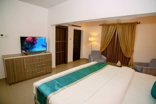 A hotel room with a bed, a TV on a wooden cabinet, a chair, and a lamp.