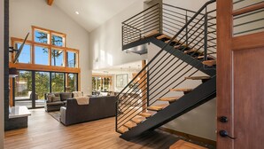 Amplia sala de estar con una escalera moderna, piso de madera y grandes ventanales que dejan entrar luz natural.