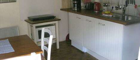 A small kitchen with a dining table and chairs, a microwave, a coffee maker, and various utensils on the counter.