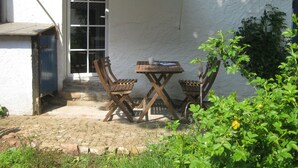 Ein kleiner Außenbereich mit Tisch und zwei Stühlen, einem Streifenmarkisen und einem Blumentopf.
