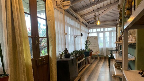 Un pasillo con suelo de baldosas, bancos de madera, plantas en macetas y un aparador de estilo antiguo.