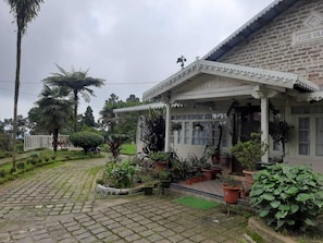 A traditional house with a porch, surrounded by lush greenery and a paved pathway. - Rose Villa British Colonial Heritage Bungalow, Takdah (Takdah)