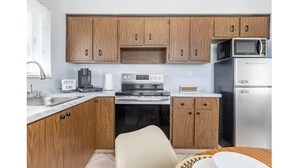 Una cocina compacta con armarios de madera, un refrigerador de acero inoxidable, un microondas, una cafetera y una estufa.