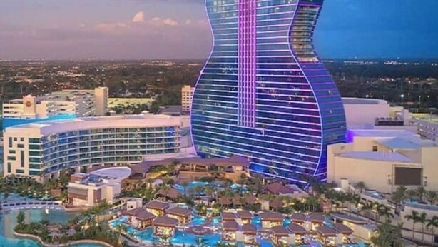 Un resort con un edificio grande con forma de guitarra, que cuenta con una piscina y varias villas para huéspedes.