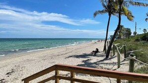 Una playa con un camino de madera que lleva a la orilla, palmeras y el océano.