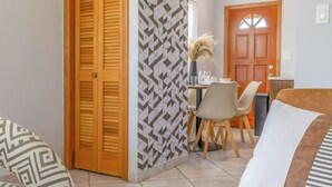 Una sala de estar con sofá, comedor con mesa y sillas, puerta de madera y papel tapiz estampado.